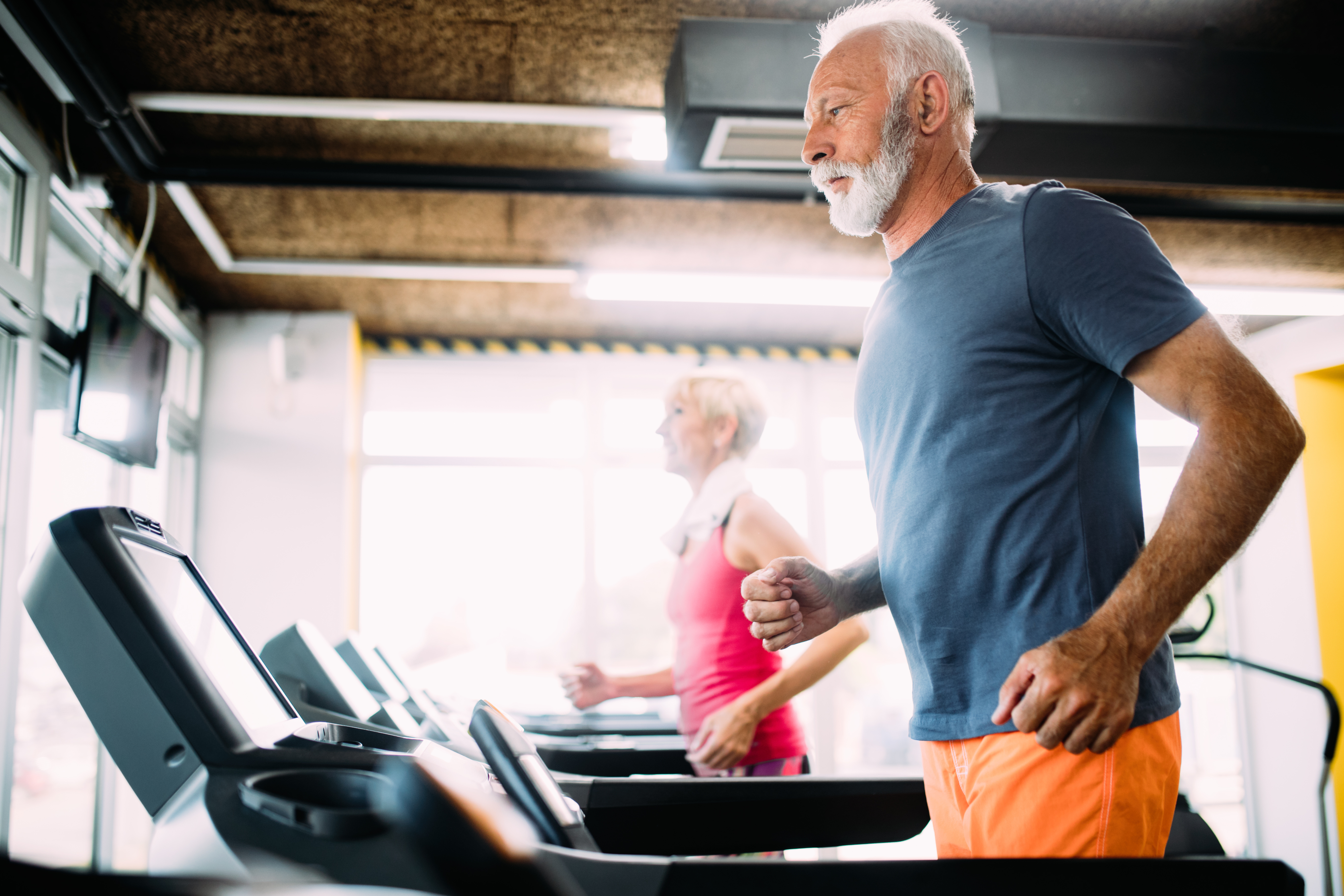 elderly man and woman running on treadmills