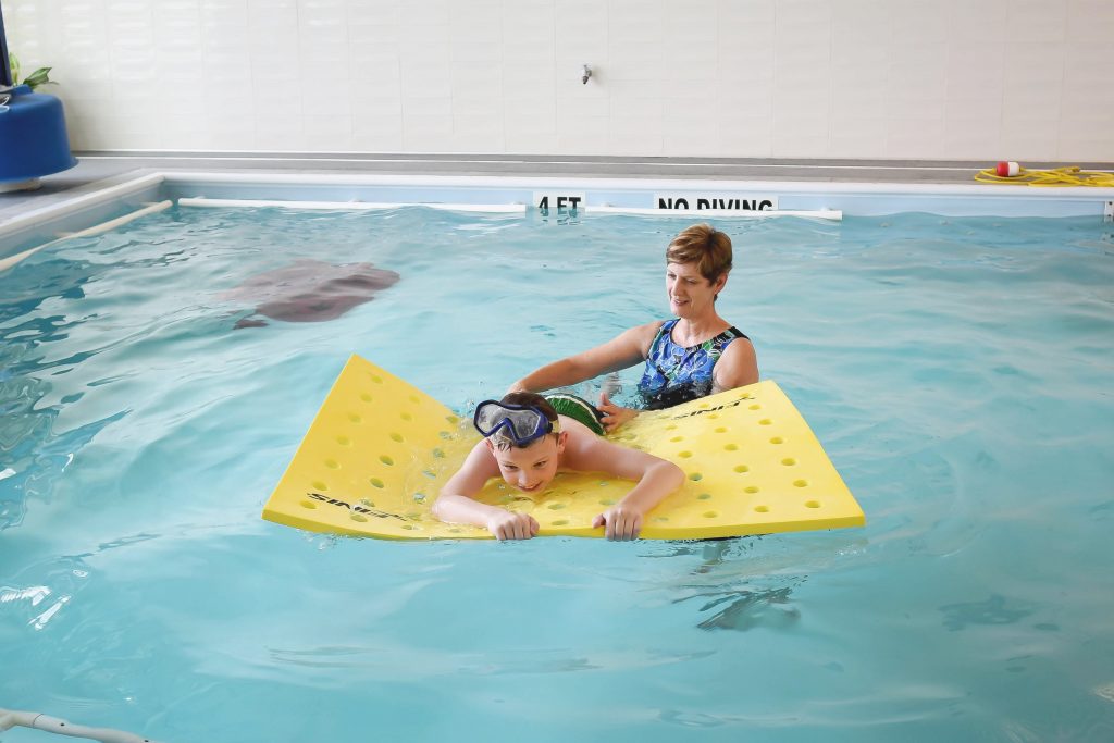 Aquatic therapist teaching a boy how to swim using a floatable