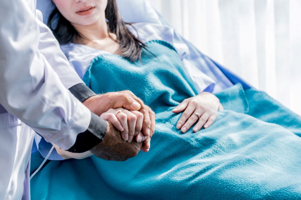 Doctor holding a young woman's hand while she is in a hospital bed