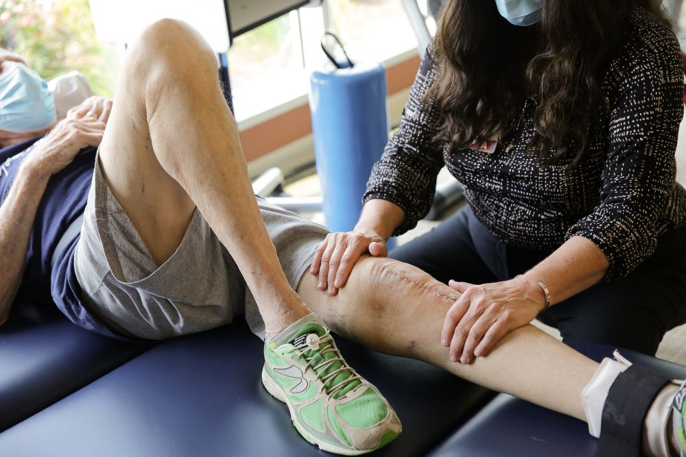 physical therapist helping patient stretch his leg after knee surgery